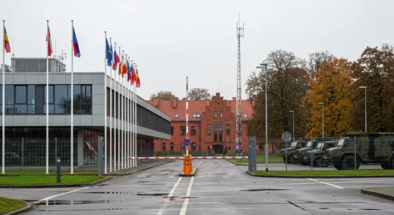Nowoczesny kompleks wielonarodowego dowodztwa wojskowego w Polsce z maszatami flagowymi, szlabanem i pojazdami wojskowym